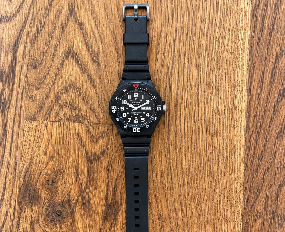 Casio MRW200H watch with black resin case and strap on a wood floor