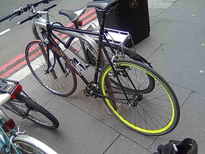 The fixed-gear bike with its yellow rear rim locked up on a city sidewalk